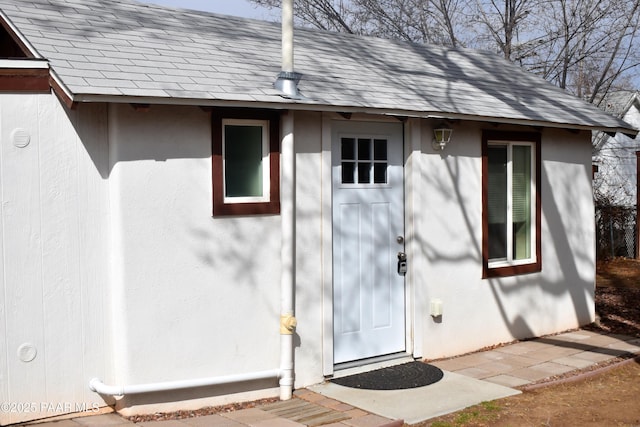 doorway to property featuring a shingled roof and stucco siding