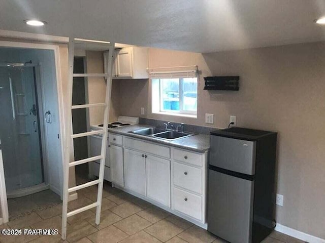 kitchen featuring baseboards, light tile patterned flooring, freestanding refrigerator, a sink, and white cabinetry