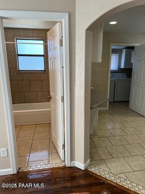 corridor with arched walkways, light tile patterned flooring, baseboards, washing machine and clothes dryer, and a textured wall