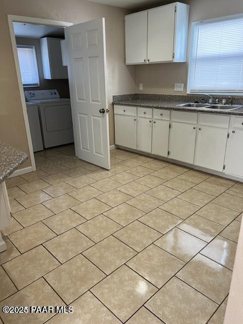 kitchen featuring washer and dryer, light tile patterned floors, baseboards, a sink, and white cabinetry