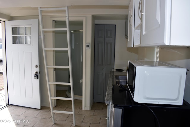 kitchen featuring white microwave, light tile patterned floors, white cabinets, and light countertops