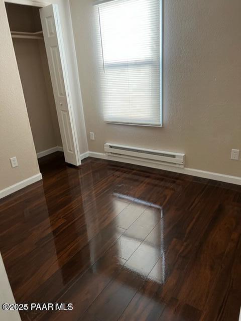 unfurnished bedroom featuring a closet, baseboards, baseboard heating, and wood finished floors