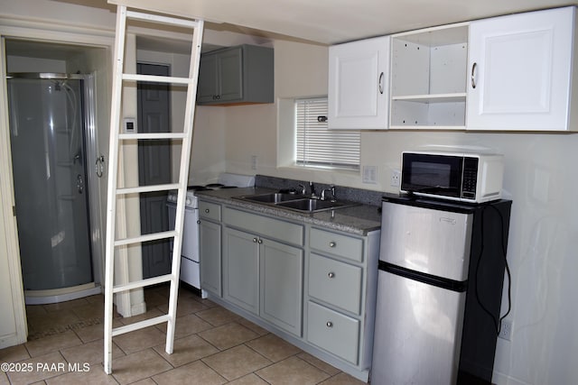 kitchen with gray cabinetry, a sink, open shelves, freestanding refrigerator, and light tile patterned floors