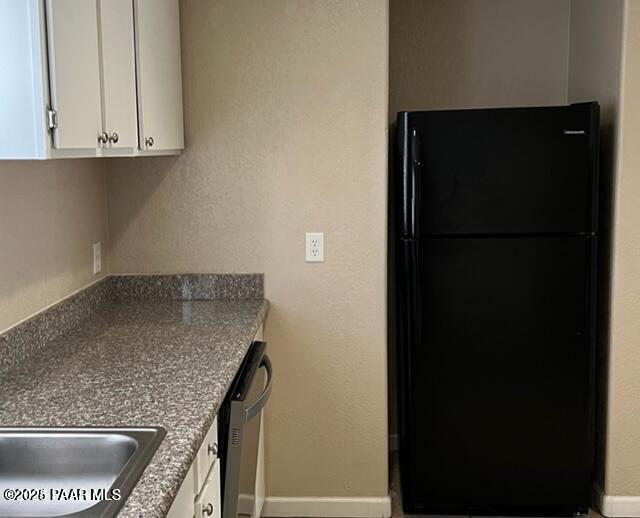 kitchen with dishwasher, white cabinets, baseboards, and freestanding refrigerator