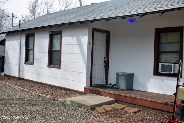 view of exterior entry featuring cooling unit and a shingled roof