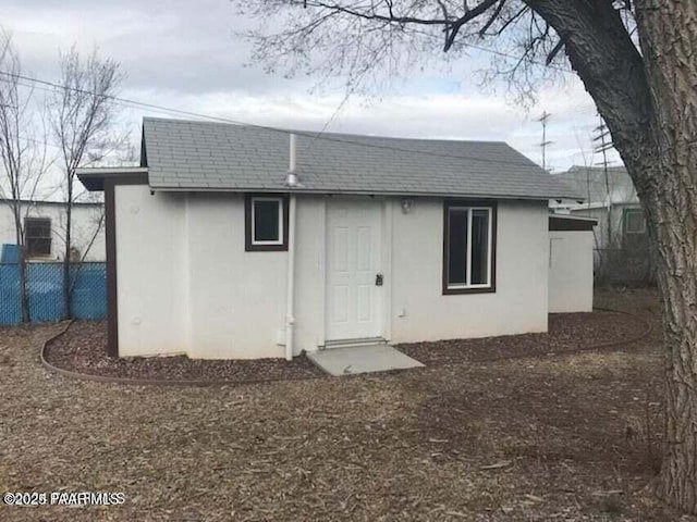 back of house with stucco siding, roof with shingles, and fence