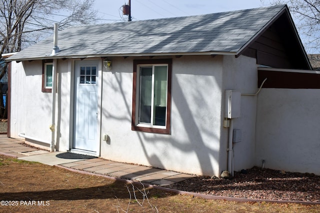 back of house with stucco siding and a shingled roof