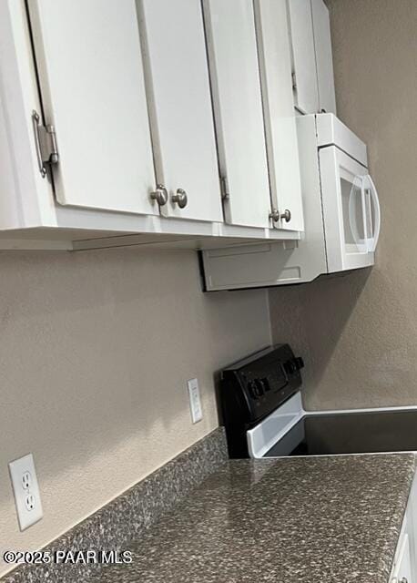 kitchen featuring white microwave, range with electric cooktop, and white cabinetry