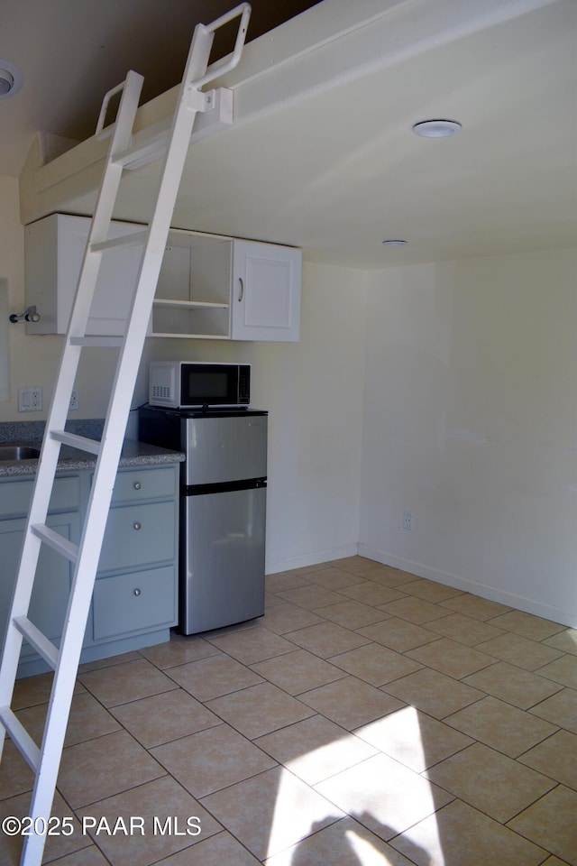 kitchen with light tile patterned floors, white cabinetry, freestanding refrigerator, and baseboards