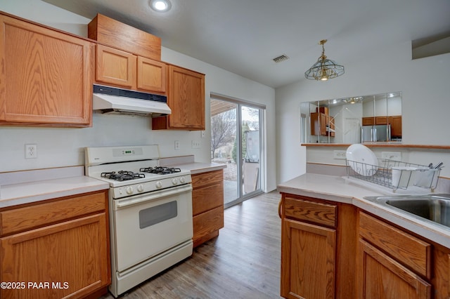 kitchen with white gas range oven, light countertops, freestanding refrigerator, under cabinet range hood, and visible vents