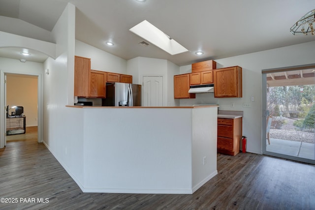 kitchen featuring visible vents, vaulted ceiling with skylight, dark wood finished floors, under cabinet range hood, and stainless steel refrigerator with ice dispenser