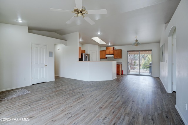 unfurnished living room with arched walkways, vaulted ceiling with skylight, ceiling fan, and wood finished floors