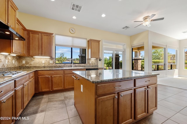 kitchen with light stone countertops, a center island, tasteful backsplash, and sink