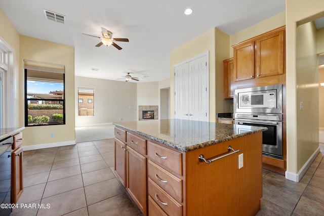 kitchen with ceiling fan, stainless steel appliances, tile patterned flooring, dark stone countertops, and a kitchen island