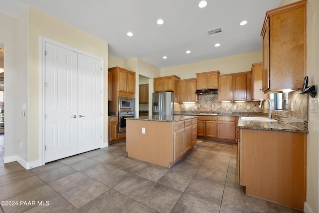 kitchen featuring backsplash, dark stone counters, stainless steel appliances, sink, and a kitchen island