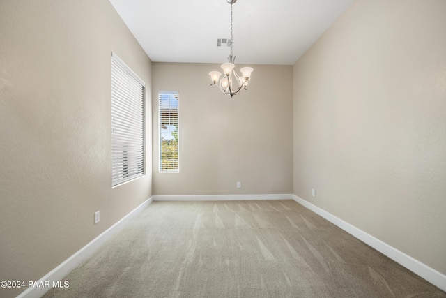 carpeted empty room featuring a notable chandelier