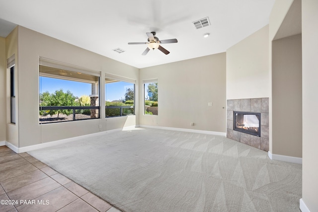 unfurnished living room with a tile fireplace, light carpet, and ceiling fan