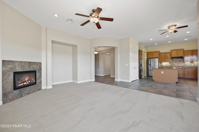 unfurnished living room featuring a fireplace, dark carpet, and ceiling fan