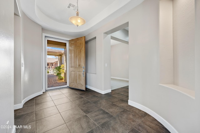 foyer with a raised ceiling and dark tile patterned floors