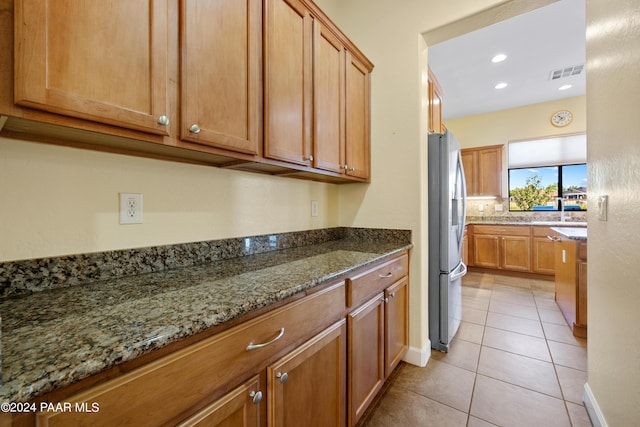 kitchen with stainless steel fridge, stone countertops, light tile patterned floors, and sink