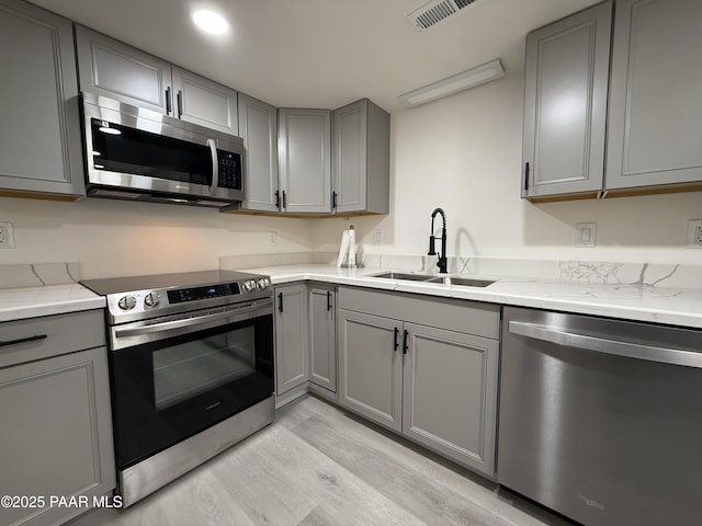 kitchen featuring appliances with stainless steel finishes, sink, gray cabinetry, light stone countertops, and light wood-type flooring