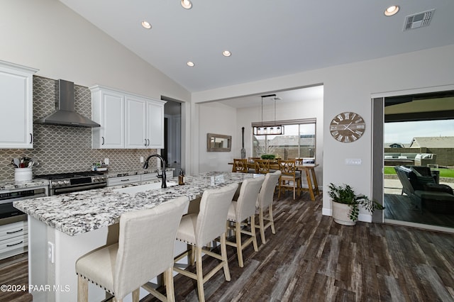 kitchen with white cabinets, a center island with sink, wall chimney exhaust hood, appliances with stainless steel finishes, and dark hardwood / wood-style flooring