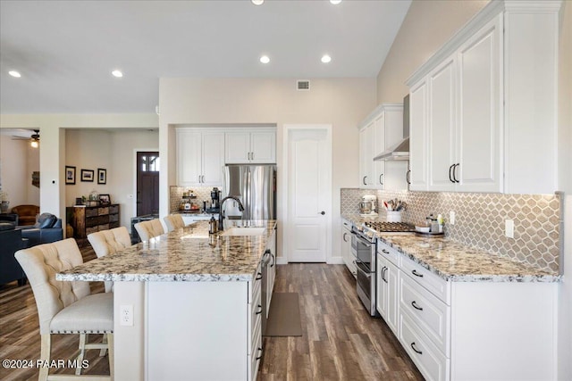 kitchen featuring dark wood-type flooring, stainless steel appliances, a kitchen island with sink, a breakfast bar, and white cabinets