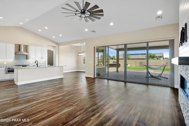 unfurnished living room featuring dark hardwood / wood-style flooring, vaulted ceiling, ceiling fan, and a stone fireplace