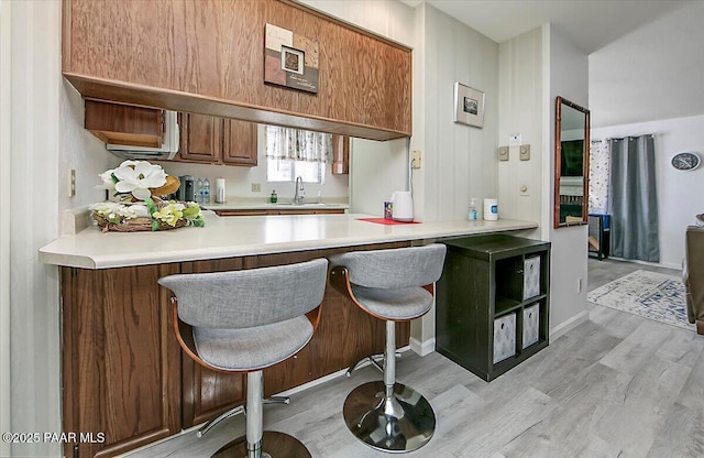 kitchen with a kitchen breakfast bar, a peninsula, light countertops, light wood-type flooring, and a sink