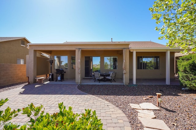 rear view of house with a patio, fence, and stucco siding