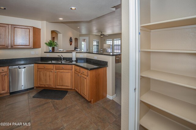 kitchen featuring ceiling fan, dishwasher, sink, kitchen peninsula, and dark stone countertops