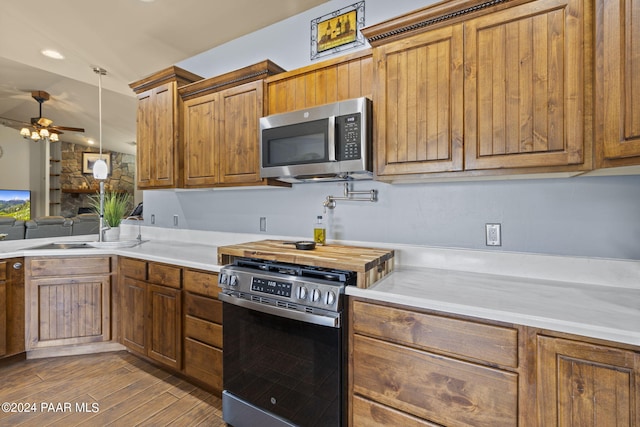 kitchen with a stone fireplace, sink, light hardwood / wood-style flooring, decorative light fixtures, and stainless steel appliances