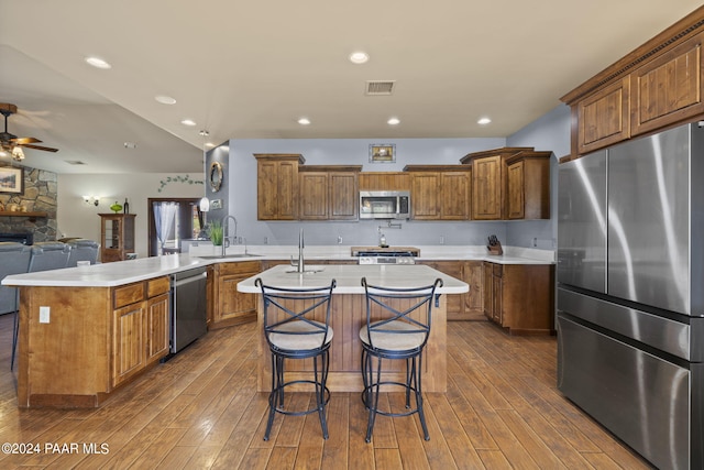 kitchen with kitchen peninsula, stainless steel appliances, dark hardwood / wood-style floors, and an island with sink