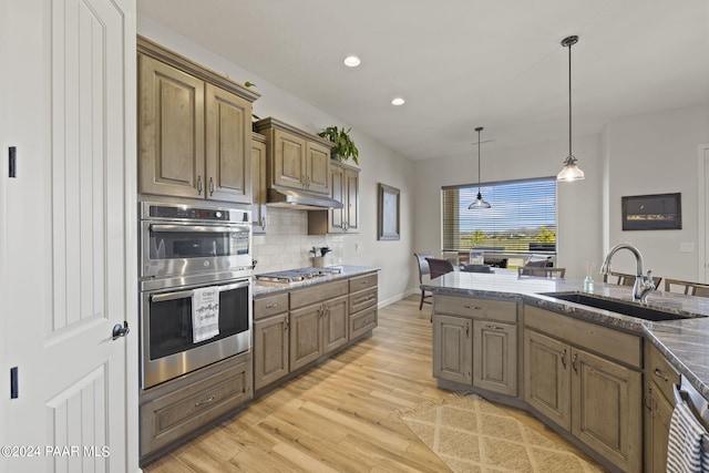 kitchen featuring sink, hanging light fixtures, backsplash, appliances with stainless steel finishes, and light wood-type flooring