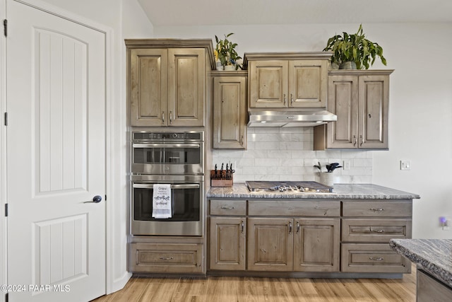 kitchen featuring tasteful backsplash, dark stone countertops, appliances with stainless steel finishes, and light hardwood / wood-style flooring