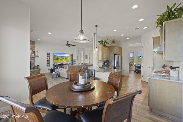 dining area featuring light wood-type flooring, a stone fireplace, ceiling fan, and sink