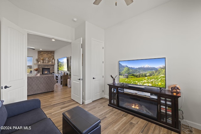 living room with ceiling fan, a stone fireplace, and light hardwood / wood-style flooring