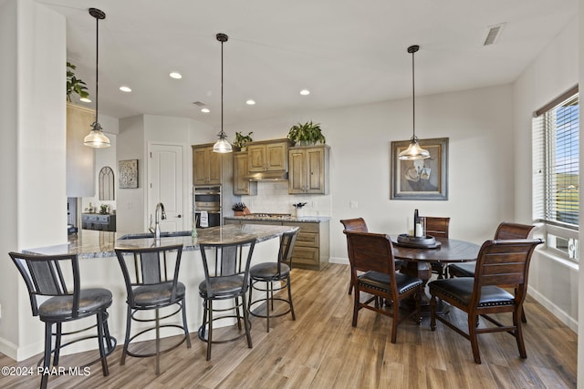 kitchen with kitchen peninsula, a kitchen breakfast bar, light wood-type flooring, tasteful backsplash, and stone counters