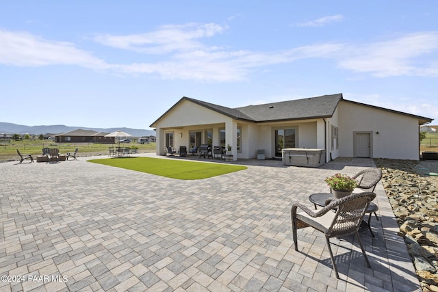 back of property featuring a mountain view, a patio, and a hot tub