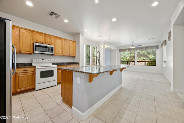 kitchen featuring ceiling fan with notable chandelier, refrigerator, white range with electric stovetop, sink, and a center island with sink