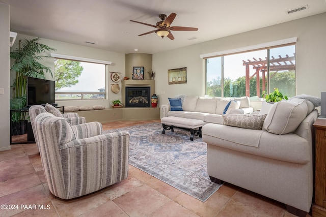 living room featuring a large fireplace, ceiling fan, and a healthy amount of sunlight