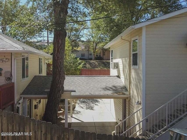 exterior space with a shingled roof, stairs, and fence