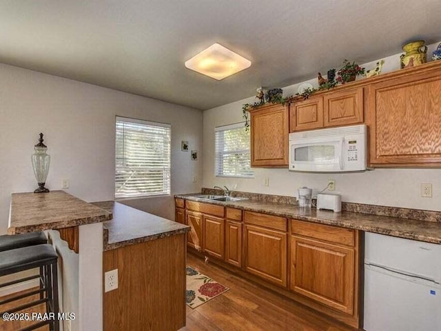 kitchen with brown cabinetry, white microwave, a sink, dark countertops, and a kitchen breakfast bar