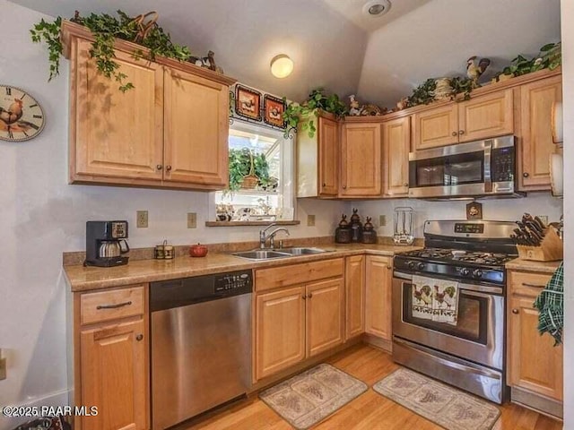 kitchen featuring a sink, stainless steel appliances, light wood-style flooring, and vaulted ceiling