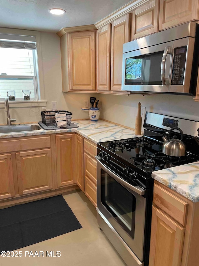 kitchen with a sink, light brown cabinets, light stone countertops, and stainless steel appliances