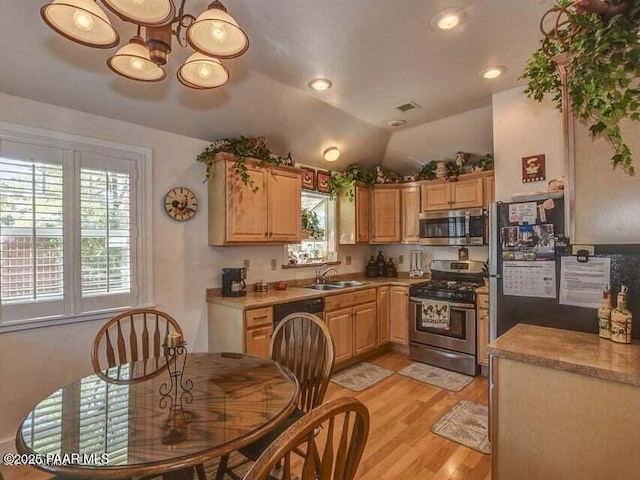 kitchen with light wood-style flooring, a sink, vaulted ceiling, appliances with stainless steel finishes, and a chandelier