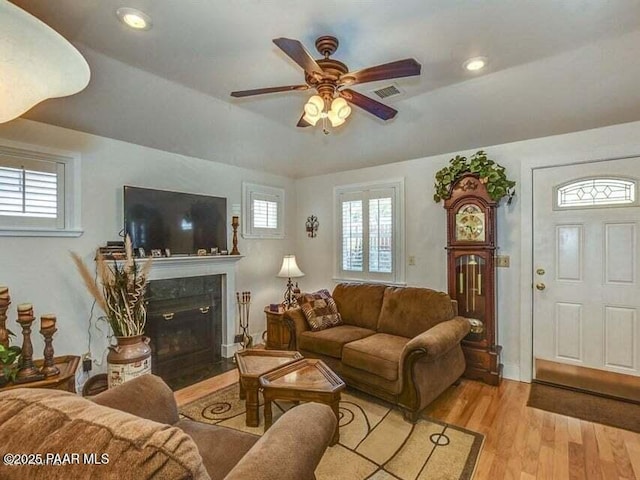 living room with visible vents, a tray ceiling, light wood finished floors, ceiling fan, and a tile fireplace