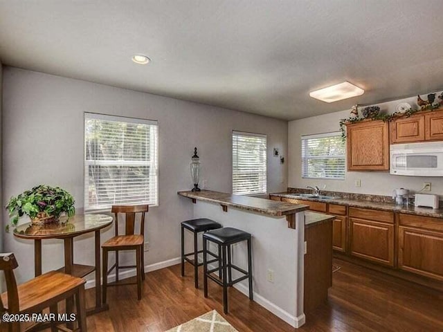 kitchen with brown cabinets, dark countertops, dark wood finished floors, a breakfast bar area, and white microwave