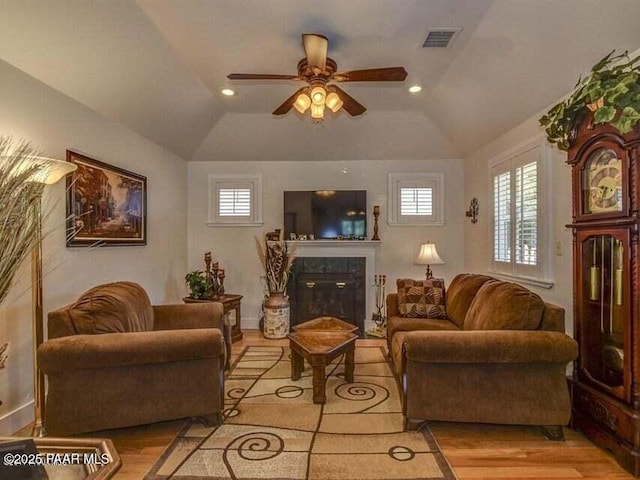 living area featuring light wood finished floors, lofted ceiling, a ceiling fan, and a tile fireplace