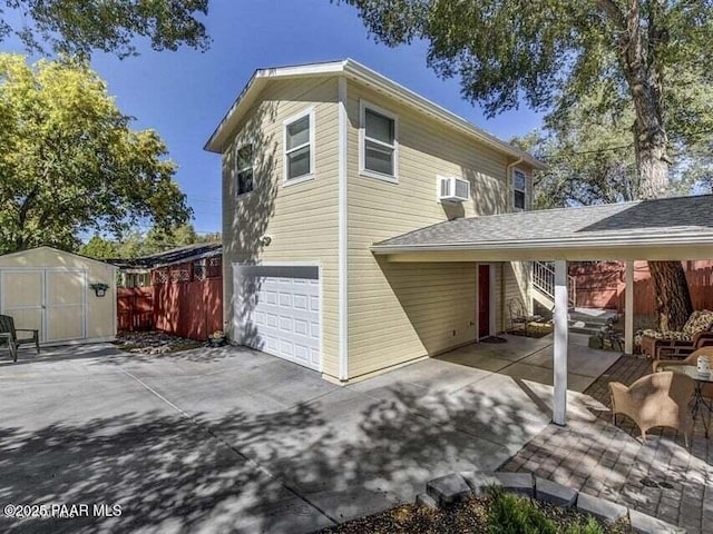 view of property exterior with an outbuilding, a wall mounted AC, fence, a storage shed, and a garage